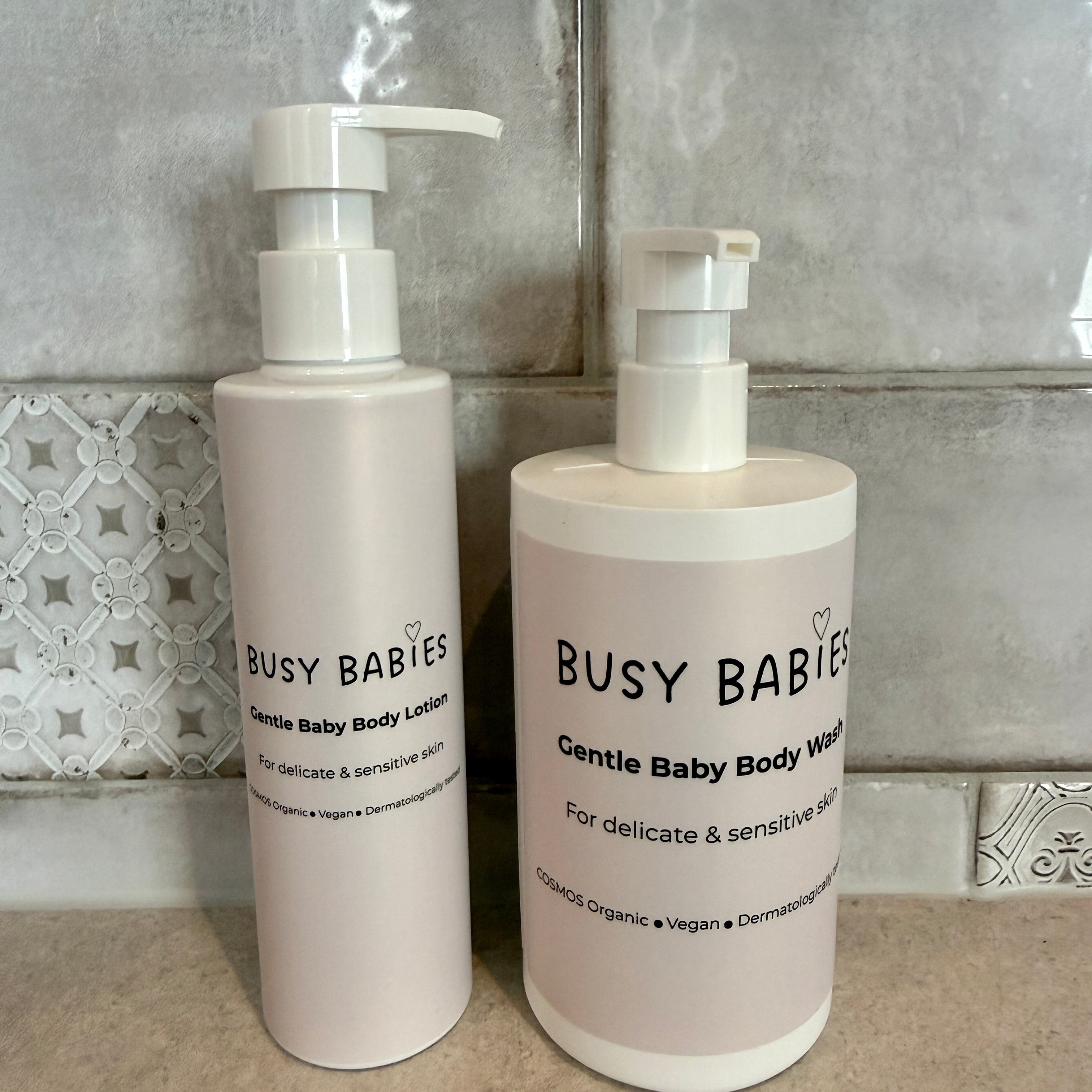 Two bottles of Busy Babies Gentle Baby Body Lotion and Body Wash on a tiled bathroom floor.