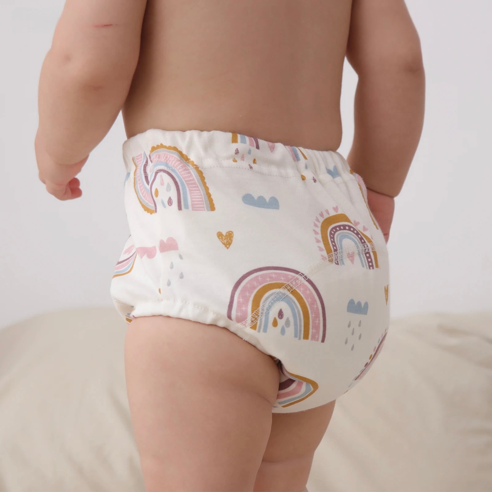 Baby wearing a Baby Cotton Reusable Training Pant with rainbow and cloud pattern on a plain background